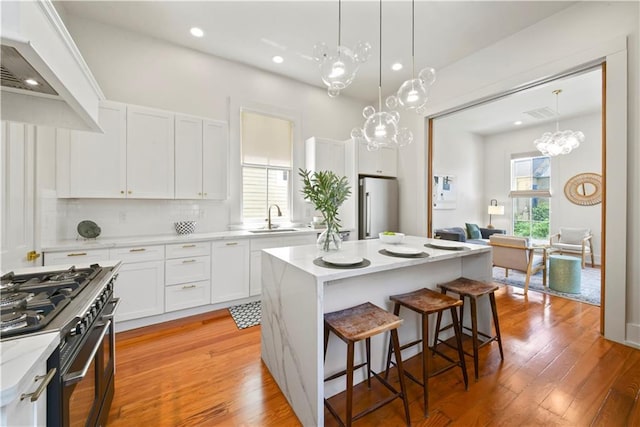 3311 Saint Ann St, New Orleans, LA 70119 - kitchen with range hood, stainless steel appliances, a chandelier, a kitchen bar, and a kitchen island