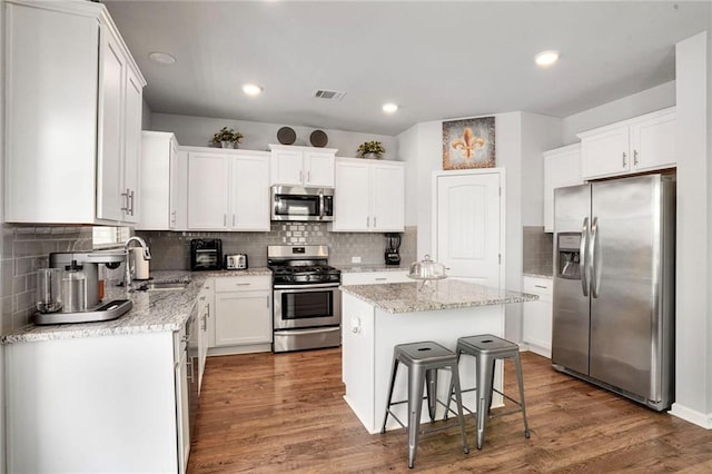 801 Lakeshore Village Dr, Slidell, LA 70461 - kitchen featuring appliances with stainless steel finishes, a kitchen island, backsplash, white cabinets, and wood finished floors