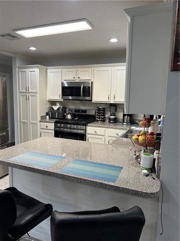 532 Deerfield Rd, Terrytown, LA 70056 - kitchen with stainless steel appliances, a kitchen bar, ornamental molding, white cabinets, and recessed lighting
