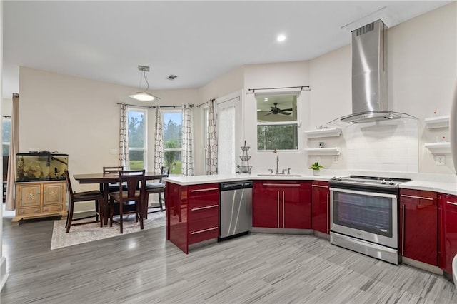 22484 Treadaway St, Mandeville, LA 70471 - kitchen featuring stainless steel appliances, wall chimney range hood, red cabinets, decorative backsplash, and a ceiling fan