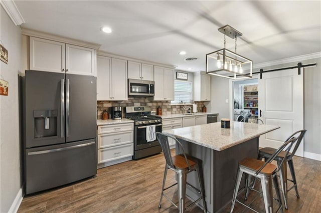 5028 Jasper St, Metairie, LA 70006 - kitchen with appliances with stainless steel finishes, washer and clothes dryer, a breakfast bar, a barn door, and tasteful backsplash