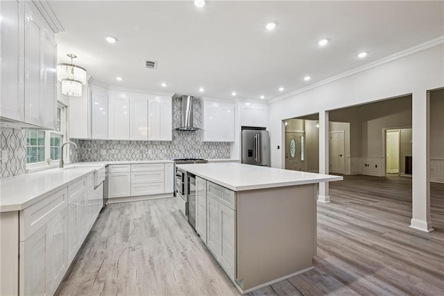325 Jasmine Dr, Mandeville, LA 70471 - kitchen with stainless steel appliances, wall chimney range hood, light wood-style floors, a kitchen island, and crown molding