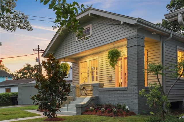 2303 Wisteria St, New Orleans, LA 70122 - view of front facade featuring brick siding, a front lawn, an outbuilding, and covered porch