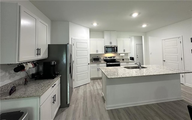 42423 Landing View Rd, Ponchatoula, LA 70454 - kitchen with stainless steel appliances, light wood-style flooring, white cabinetry, light stone countertops, and an island with sink