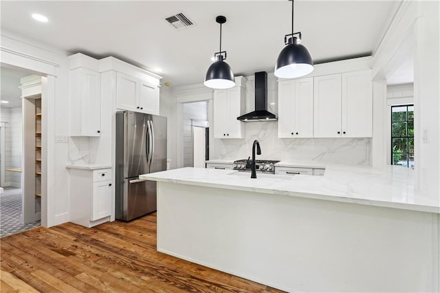 72287 Military Rd, Covington, LA 70435 - kitchen with wall chimney range hood, freestanding refrigerator, wood finished floors, white cabinetry, and tasteful backsplash