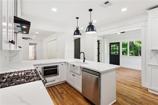 72287 Military Rd, Covington, LA 70435 - kitchen featuring stainless steel appliances, ventilation hood, wood finished floors, white cabinets, and pendant lighting