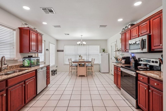 70105 10th St, Covington, LA 70433 - kitchen with stainless steel appliances, reddish brown cabinets, a chandelier, recessed lighting, and hanging light fixtures