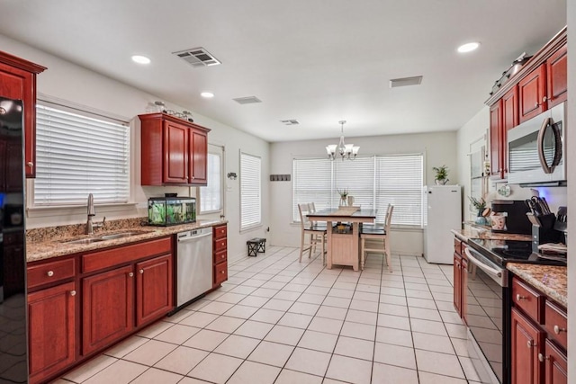 70105 10th St, Covington, LA 70433 - kitchen with stainless steel appliances, reddish brown cabinets, a chandelier, decorative light fixtures, and recessed lighting