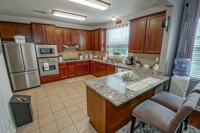 784 Lakeview Ln, Covington, LA 70435 - kitchen with appliances with stainless steel finishes, a peninsula, decorative backsplash, under cabinet range hood, and light tile patterned floors