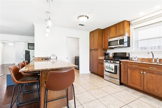 3514 Bore St, Metairie, LA 70001 - kitchen featuring appliances with stainless steel finishes, brown cabinets, a peninsula, a breakfast bar, and light stone counters