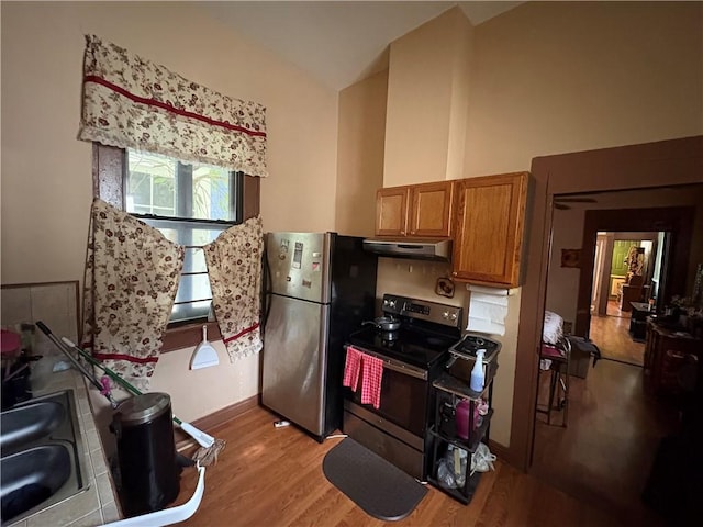 3120 Urquhart St, New Orleans, LA 70117 - kitchen with stainless steel appliances, lofted ceiling, brown cabinets, light wood-style flooring, and under cabinet range hood