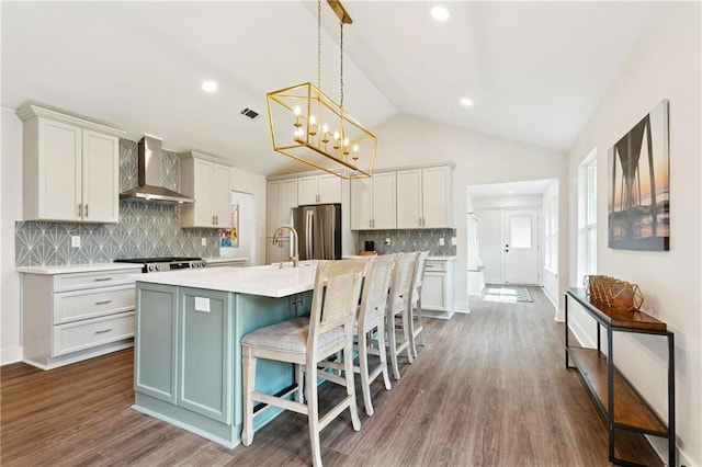 1109 Manson St, Metairie, LA 70001 - kitchen featuring wall chimney exhaust hood, freestanding refrigerator, light countertops, lofted ceiling, and a center island with sink