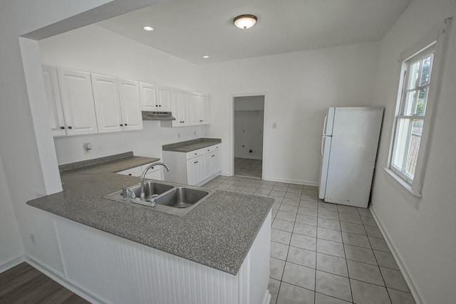 425 Park Blvd, New Orleans, LA 70114 - kitchen featuring freestanding refrigerator, under cabinet range hood, a peninsula, white cabinetry, and light tile patterned floors