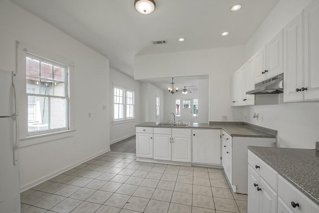 425 Park Blvd, New Orleans, LA 70114 - kitchen featuring under cabinet range hood, freestanding refrigerator, a peninsula, a chandelier, and white cabinets
