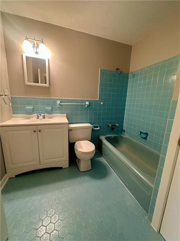 8732 25th St, Metairie, LA 70003 - bathroom with washtub / shower combination, tile walls, vanity, tile patterned floors, and wainscoting