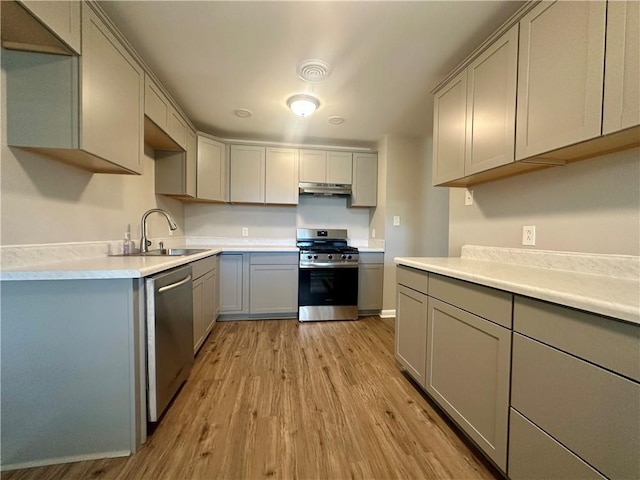 8732 25th St, Metairie, LA 70003 - kitchen featuring appliances with stainless steel finishes, gray cabinetry, light wood finished floors, under cabinet range hood, and light countertops
