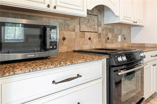 26 Chamale Cv Unit 26, Slidell, LA 70460 - kitchen with black range with electric stovetop, stainless steel microwave, stone countertops, white cabinets, and tasteful backsplash
