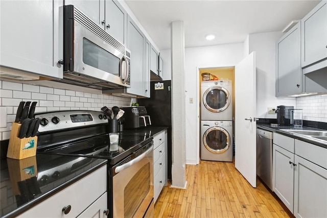 920 Poeyfarre St Unit 326, New Orleans, LA 70130 - kitchen featuring stainless steel appliances, stacked washer / drying machine, dark countertops, light wood-style floors, and decorative backsplash