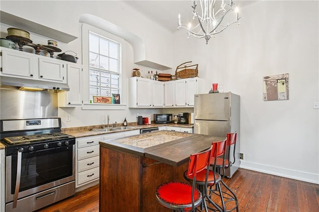 1821 Urquhart St, New Orleans, LA 70116 - kitchen with stainless steel appliances, under cabinet range hood, white cabinets, dark wood finished floors, and a center island