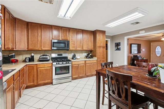 212 7th St, Bridge City, LA 70094 - kitchen featuring stainless steel appliances, backsplash, light countertops, light tile patterned floors, and crown molding