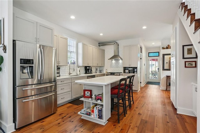 827 Port St, New Orleans, LA 70117 - kitchen with stainless steel refrigerator with ice dispenser, a breakfast bar area, light countertops, tasteful backsplash, and wall chimney exhaust hood