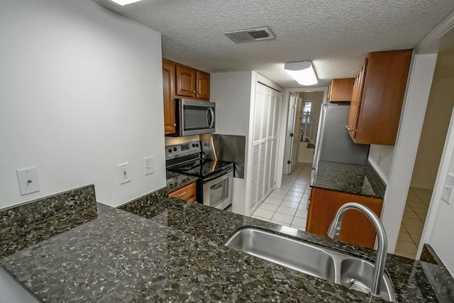 3320 Taft Park Unit C, Metairie, LA 70002 - kitchen with appliances with stainless steel finishes, brown cabinetry, light tile patterned flooring, dark stone countertops, and a textured ceiling