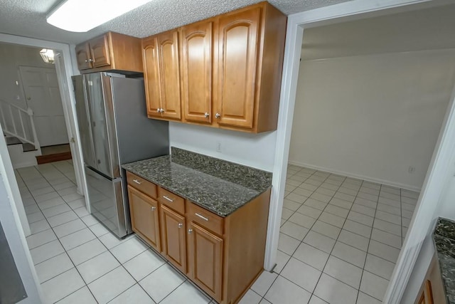 3320 Taft Park Unit C, Metairie, LA 70002 - kitchen with light tile patterned floors, dark stone countertops, brown cabinetry, freestanding refrigerator, and a textured ceiling