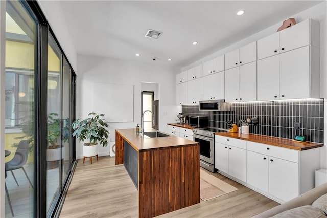2113 Harmony St, New Orleans, LA 70115 - kitchen featuring butcher block counters, stainless steel appliances, backsplash, light wood-type flooring, and an island with sink