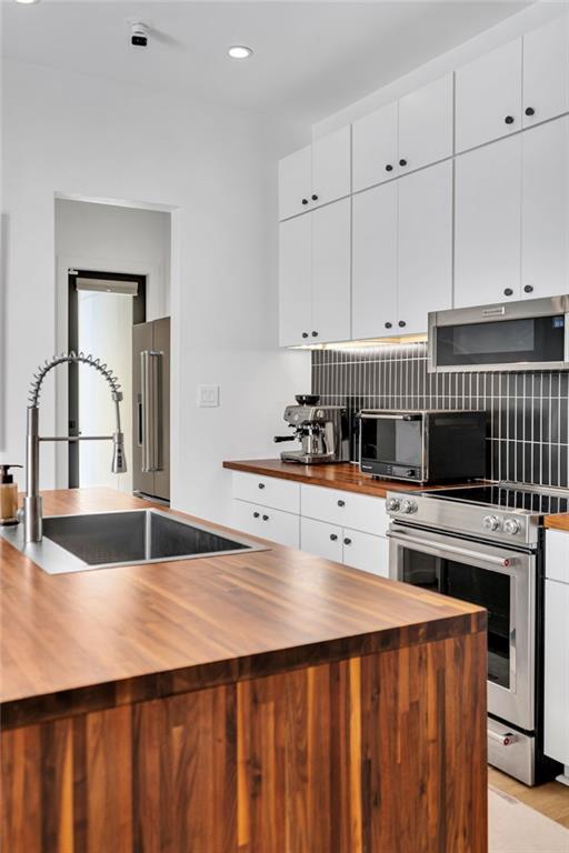 2113 Harmony St, New Orleans, LA 70115 - kitchen featuring wooden counters, appliances with stainless steel finishes, decorative backsplash, white cabinetry, and recessed lighting