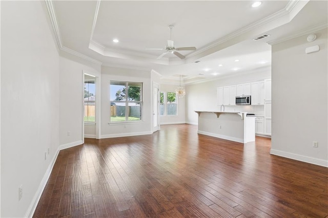 1217 N Starrett Rd, Metairie, LA 70003 - unfurnished living room featuring dark wood-type flooring, a ceiling fan, a chandelier, a tray ceiling, and crown molding