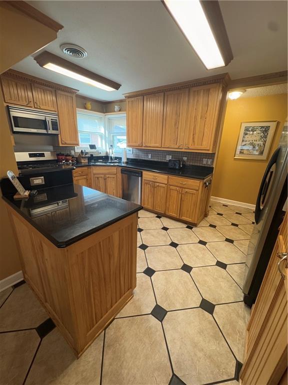 1620 Kent Ave, Metairie, LA 70001 - kitchen featuring a peninsula, appliances with stainless steel finishes, dark countertops, light tile patterned floors, and backsplash