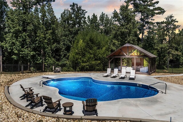 pool at dusk with a fenced in pool, a patio, fence, a gazebo, and a diving board