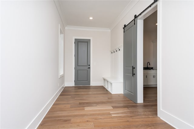 corridor with a barn door, ornamental molding, and light hardwood / wood-style flooring