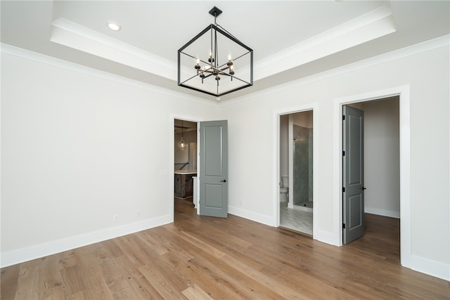 interior space with wood-type flooring, a raised ceiling, ensuite bath, and crown molding