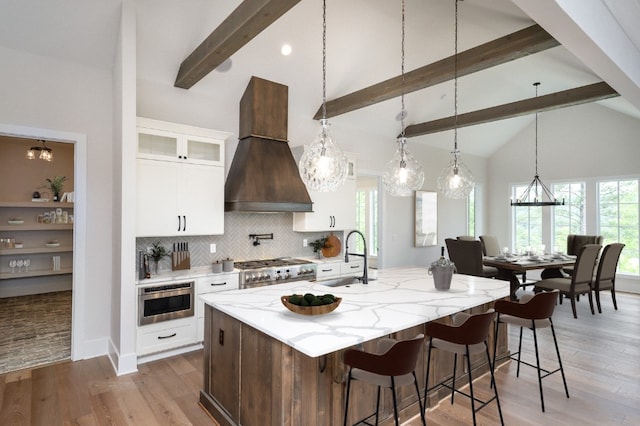 kitchen with beamed ceiling, sink, a center island with sink, custom range hood, and light wood-type flooring