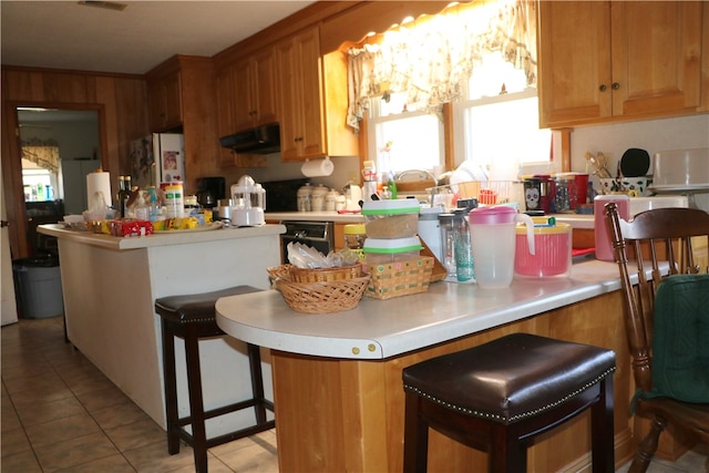 kitchen with light tile patterned flooring, white refrigerator, a breakfast bar, black dishwasher, and ventilation hood