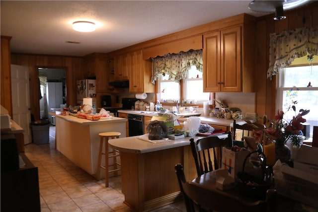 kitchen featuring a kitchen breakfast bar, kitchen peninsula, wood walls, exhaust hood, and black appliances