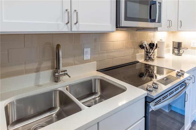 kitchen with white cabinets, stainless steel appliances, a sink, backsplash, and light countertops