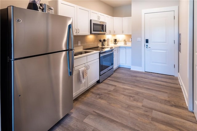 kitchen with stainless steel appliances, backsplash, white cabinetry, wood finished floors, and light countertops