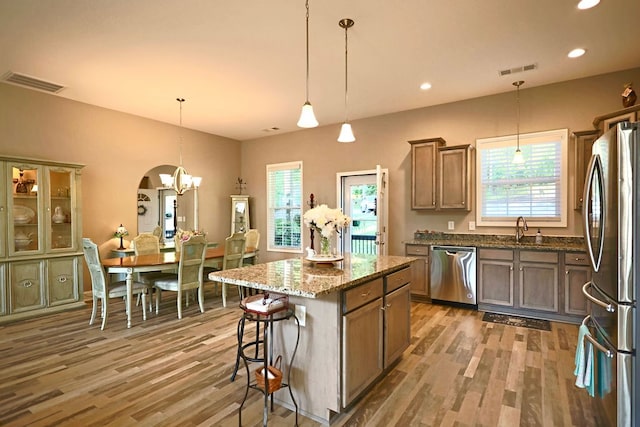 kitchen with hanging light fixtures, a kitchen island, hardwood / wood-style flooring, appliances with stainless steel finishes, and dark stone countertops