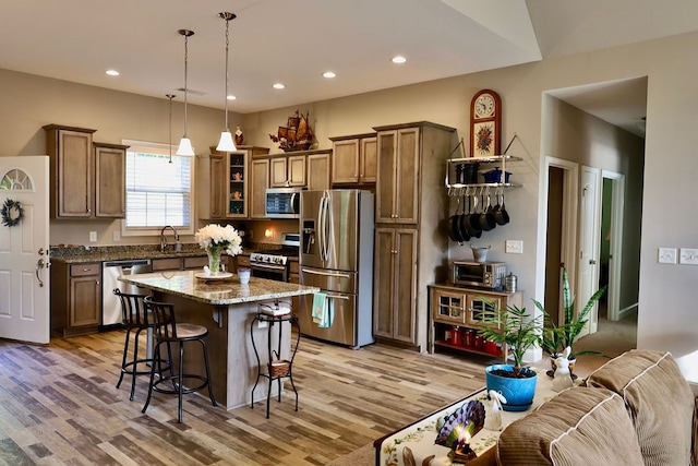 kitchen with appliances with stainless steel finishes, a breakfast bar, light stone countertops, a center island, and light hardwood / wood-style flooring