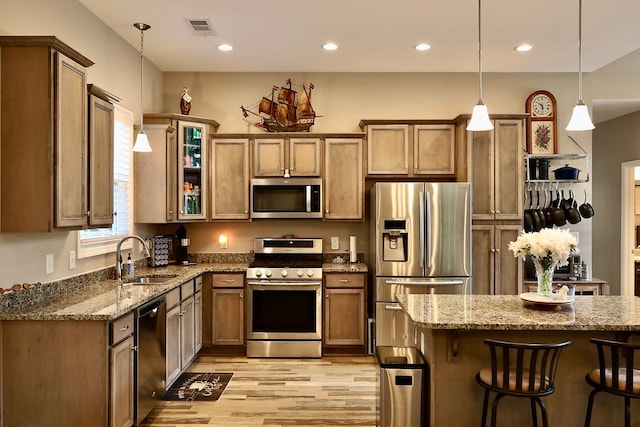 kitchen featuring appliances with stainless steel finishes, pendant lighting, light wood-type flooring, a kitchen bar, and sink