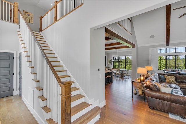 stairway featuring beam ceiling, a chandelier, high vaulted ceiling, and hardwood / wood-style flooring