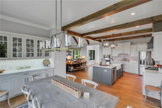 kitchen featuring light hardwood / wood-style flooring, decorative light fixtures, a kitchen island with sink, and tasteful backsplash