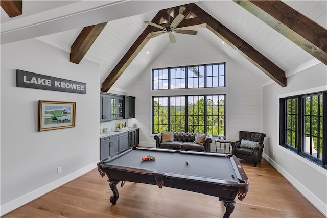 rec room featuring light wood-type flooring, ceiling fan, beamed ceiling, and bar area