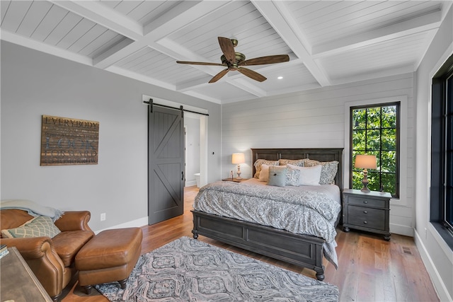 bedroom featuring light wood-type flooring, beam ceiling, coffered ceiling, a barn door, and ceiling fan