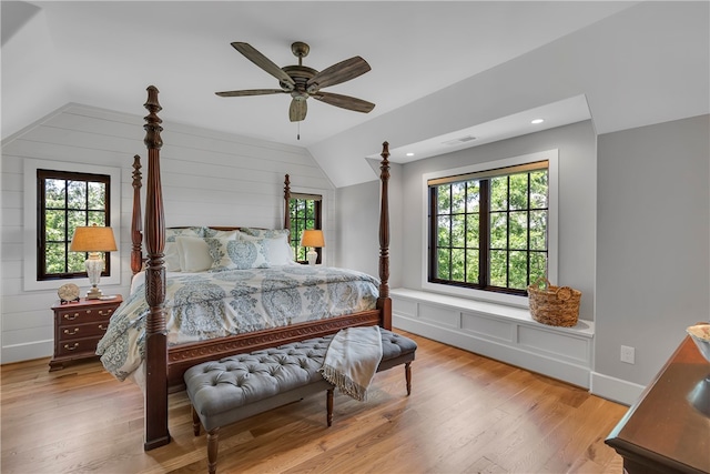 bedroom with lofted ceiling, wood walls, ceiling fan, and light hardwood / wood-style flooring