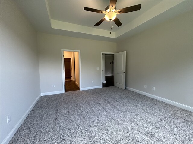 unfurnished bedroom featuring a tray ceiling, ceiling fan, and dark carpet