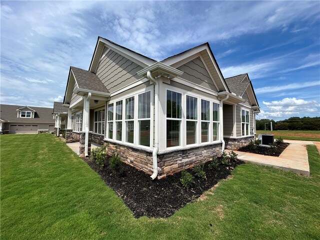 view of side of home featuring a garage, a sunroom, central AC unit, and a yard