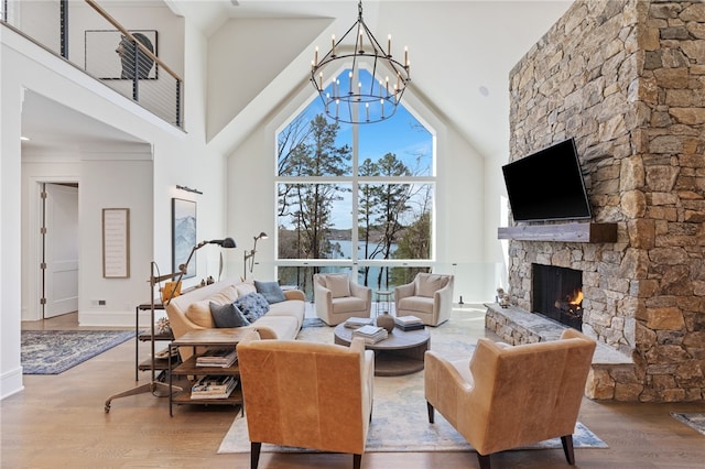 living room with a high ceiling, a stone fireplace, a notable chandelier, and hardwood / wood-style floors